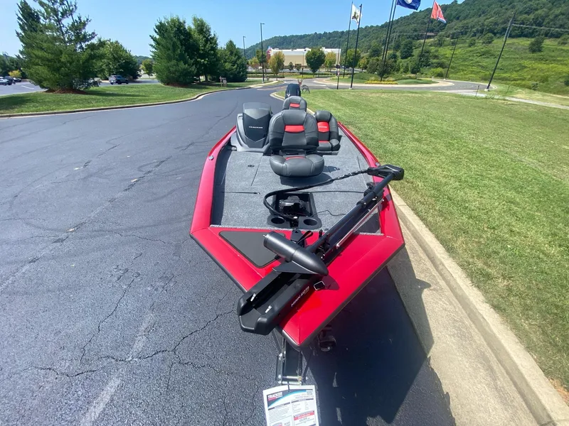 Slide: The Image of 2025 Tracker Pro Team 175 boat, red exterior, parked on asphalt near grassy area. - 6