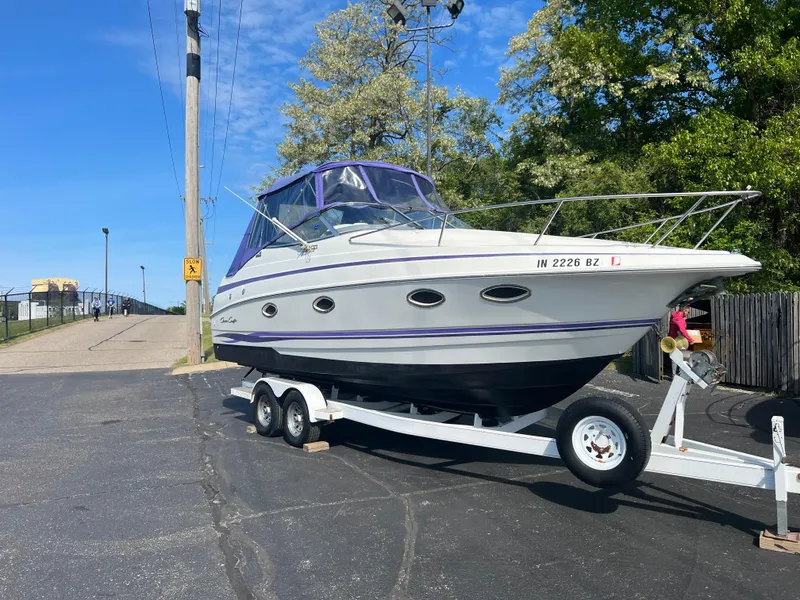 The Image of 1997 Chris-Craft 26 Crowne Cruiser on trailer, parked outdoors under clear blue sky. - 1