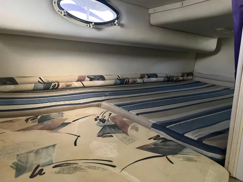 Slide: The Image of 1997 Chris-Craft 26 Crowne Cruiser cabin interior with patterned bedding and porthole window. - 12