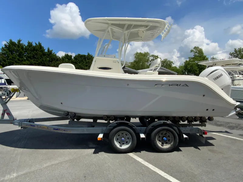 Slide: The Image of 2025 Cobia 220 Center Console boat on trailer, parked outdoors under a clear blue sky. - 6