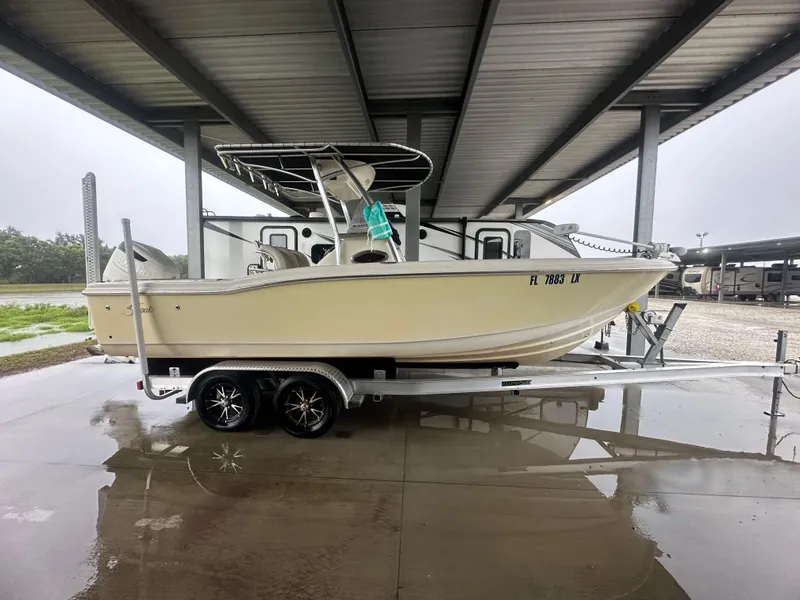 The Image of 2002 Scout 235 Sportfish boat with 2024 trailer and 2018 Suzuki 250 engine, parked under shelter. - 1
