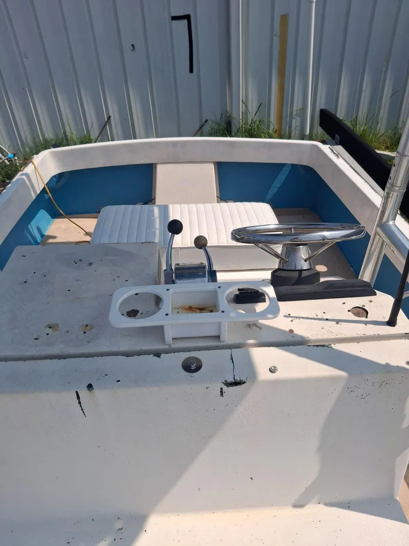 Slide: The Image of 1976 Shamrock Open Motorboat with white seating and control panel, docked near a metal building. - 4