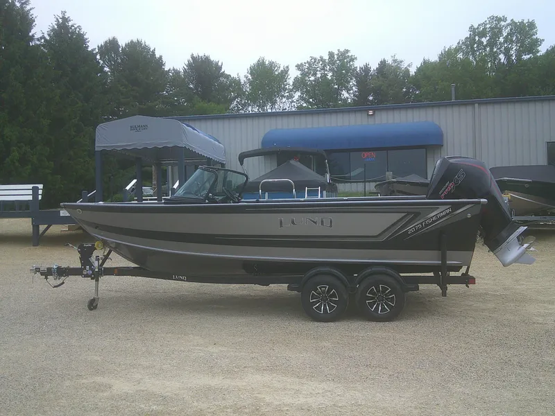The Image of 2025 Lund 2075 Fisherman boat on trailer, parked outdoors near a building. - 1