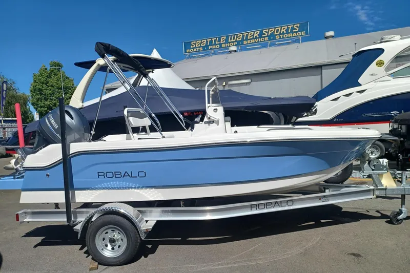 The Image of 2026 Robalo R160 Center Console boat on trailer, blue and white design, outdoor display. - 0