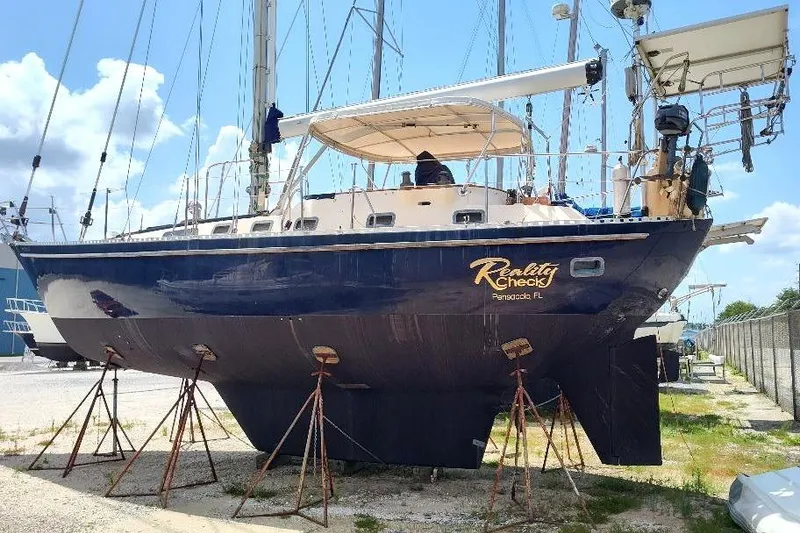 Slide: The Image of 1985 Tayana Vancover 42 sailboat on stands, named "Reality Check," in a boatyard. - 6