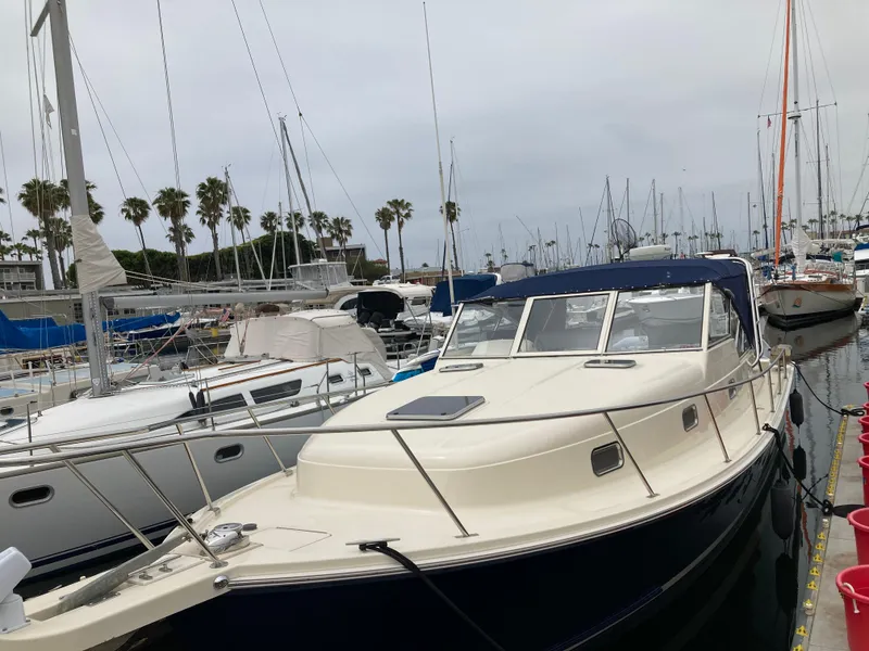 Slide: The Image of 2004 Mainship Pilot 34 docked at a marina, surrounded by sailboats and palm trees. - 2