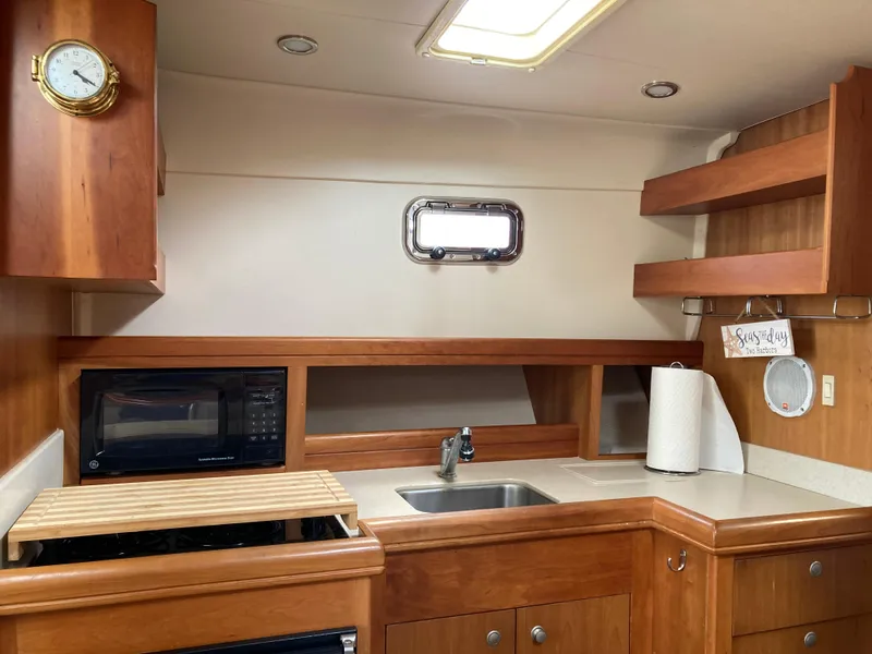 Slide: The Image of 2004 Mainship Pilot 34 kitchen with wood cabinetry, sink, microwave, and porthole window. - 28
