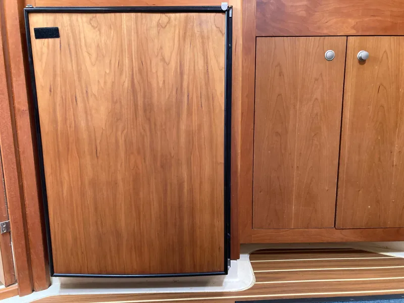 Slide: The Image of 2004 Mainship Pilot 34 interior with wooden cabinetry and compact refrigerator. - 32