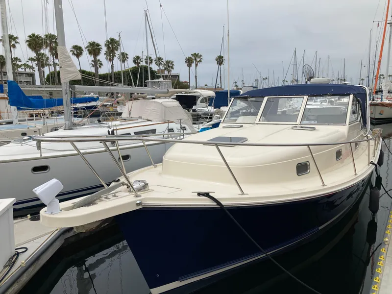 Slide: The Image of 2004 Mainship Pilot 34 docked in marina, surrounded by sailboats and palm trees. - 4