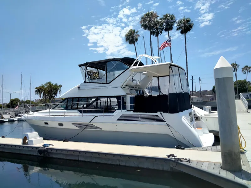 Slide: The Image of 1990 Bayliner 4387 Aft Cabin yacht docked at marina with palm trees and American flag. - 2