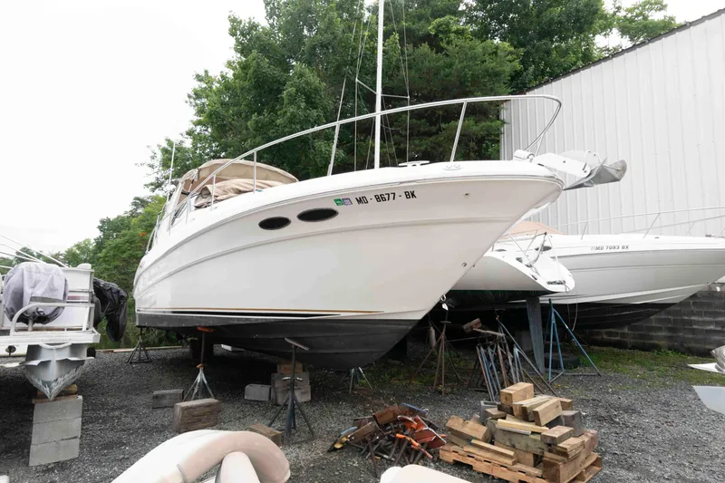 The Image of 2001 Sea Ray 340 Sundancer boat on dry dock, surrounded by trees and other boats. - 0