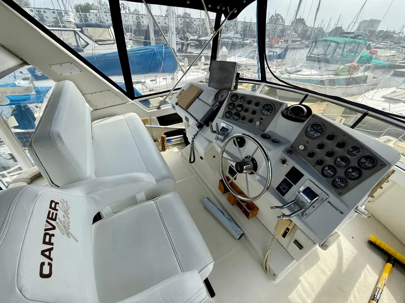 Slide: The Image of 1997 Carver 355 Aft Cabin helm with white seats and control panel in marina setting. - 10
