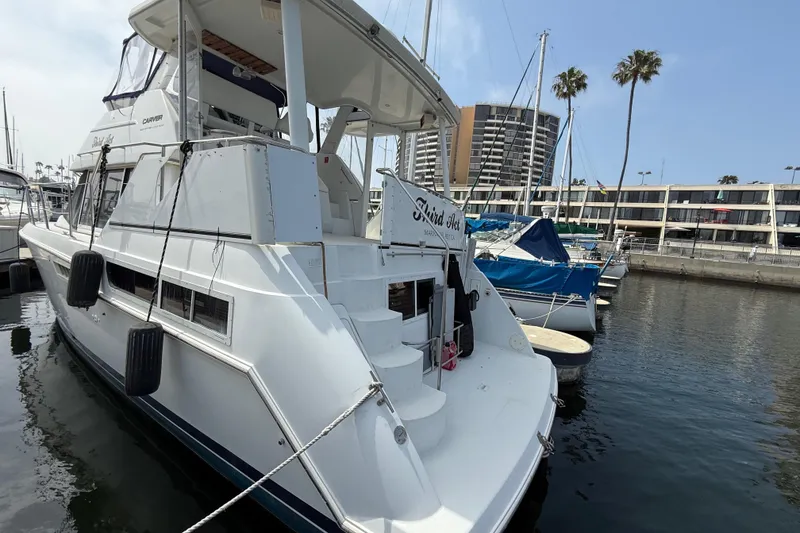 Slide: The Image of 1997 Carver 355 Aft Cabin yacht docked in marina, surrounded by other boats and palm trees. - 4