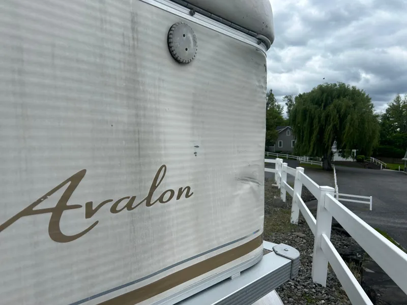 Slide: The Image of 2007 Avalon Windjammer 18' boat with dented side, parked near white fence and trees. - 7