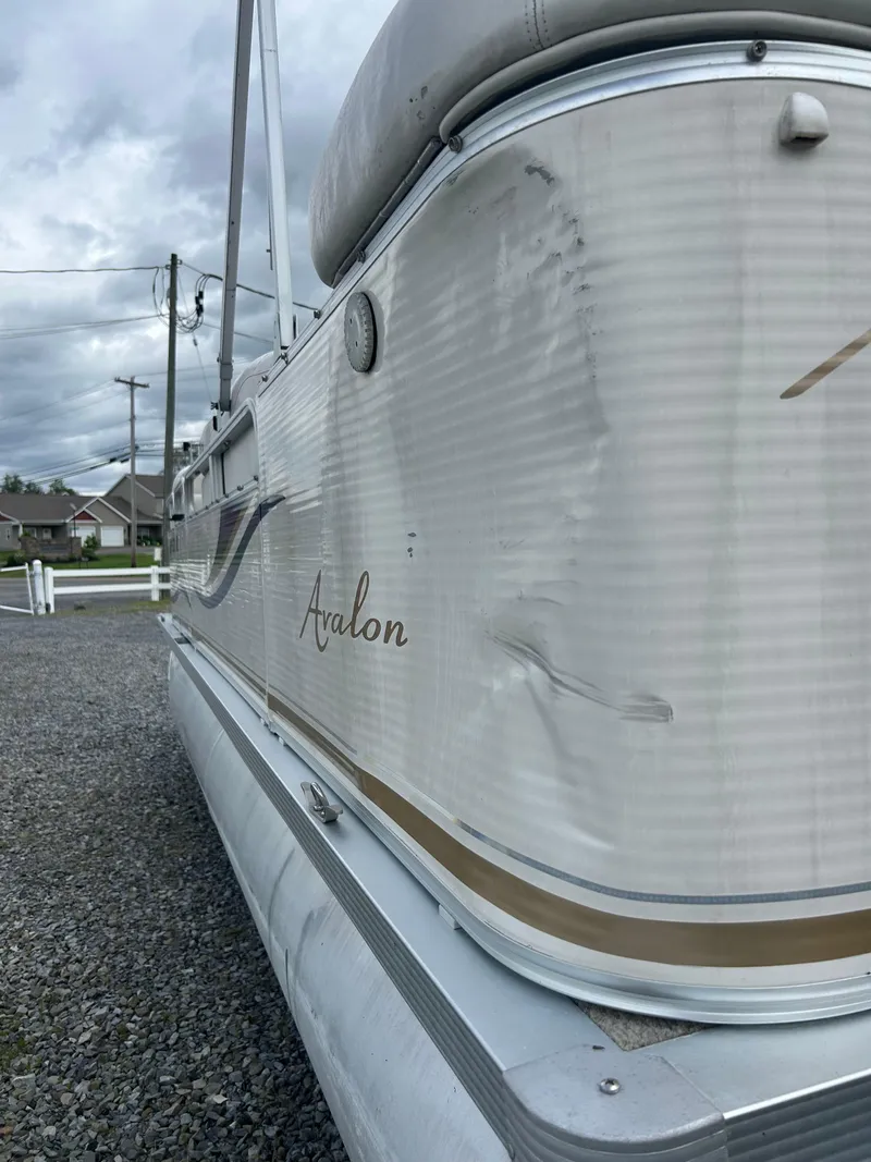 Slide: The Image of 2007 Avalon Windjammer 18' pontoon boat with visible side dent, parked on gravel. - 8
