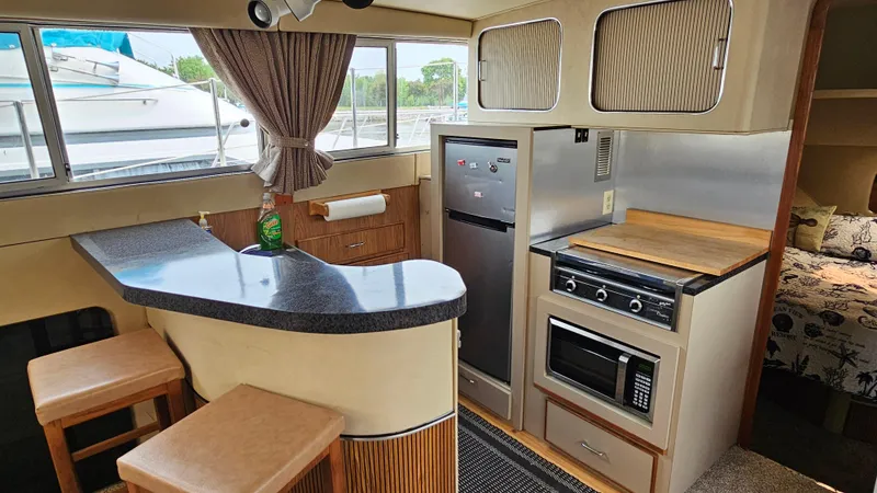 Slide: The Image of 1986 Chris-Craft 381 Catalina interior with kitchen, bar stools, and appliances. - 13