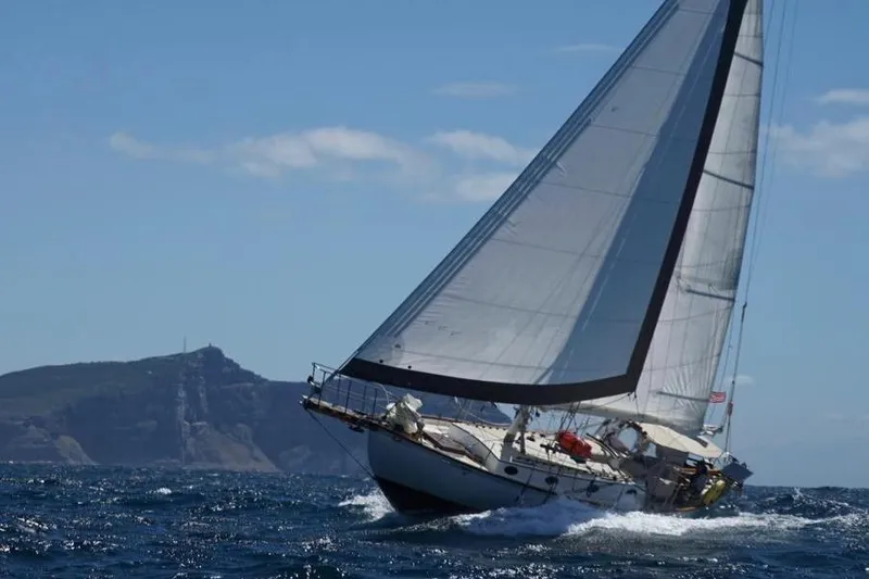 The Image of Sailing yacht Alajuela 38 Mk1, 1977, navigating ocean waves near a rocky coastline. - 0