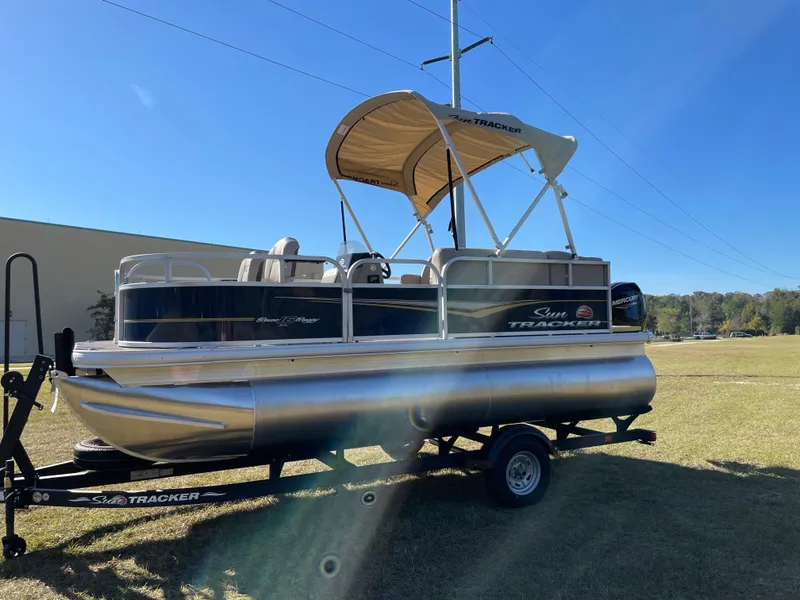 Slide: The Image of 2025 Sun Tracker Bass Buggy 16 XL Select pontoon boat on trailer, sunny day. - 2