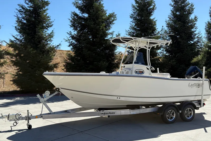 Slide: The Image of 2025 Mako 214 Center Console boat on trailer, parked outdoors with trees in background. - 5