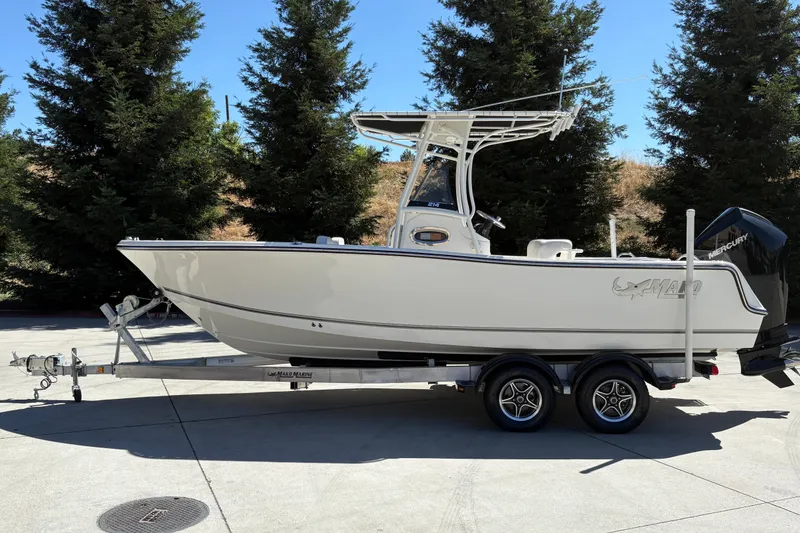 Slide: The Image of 2025 Mako 214 Center Console boat on trailer, parked outdoors with trees in background. - 1