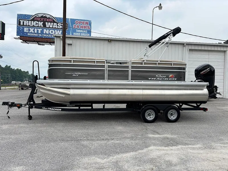 The Image of 2025 Sun Tracker Party Barge 20 DLX pontoon boat on trailer, parked near a truck wash. - 1