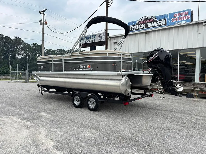 Slide: The Image of 2025 Sun Tracker Party Barge 20 DLX pontoon boat on trailer, parked near a truck wash. - 4