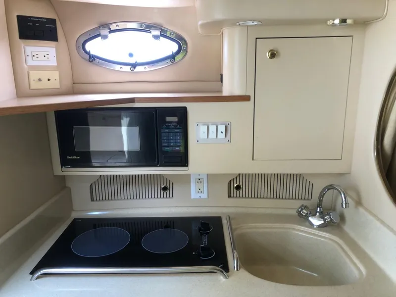 Slide: The Image of 1998 Sea Ray 290 Sundancer galley with microwave, stove, sink, and porthole window. - 7