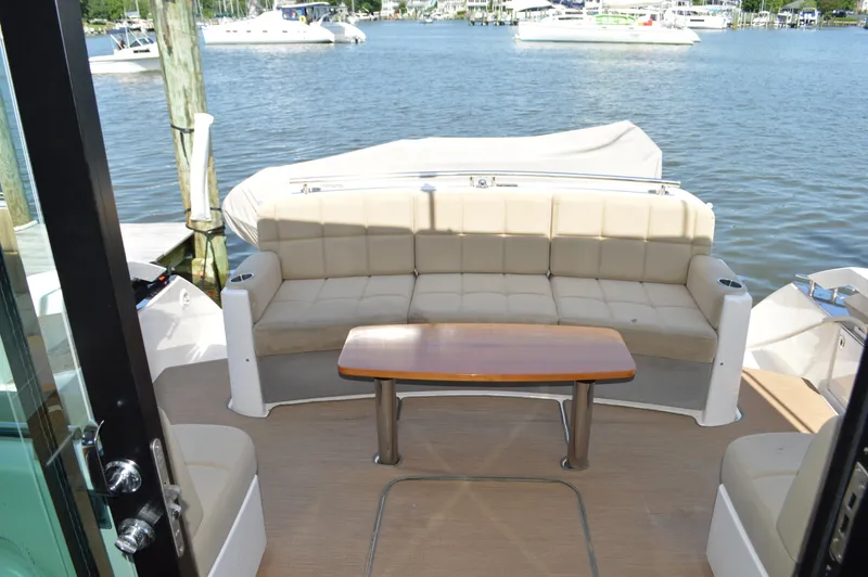 Slide: The Image of 2016 Tiara Yachts C44 Coupe interior with beige seating and wooden table, docked by the water. - 13