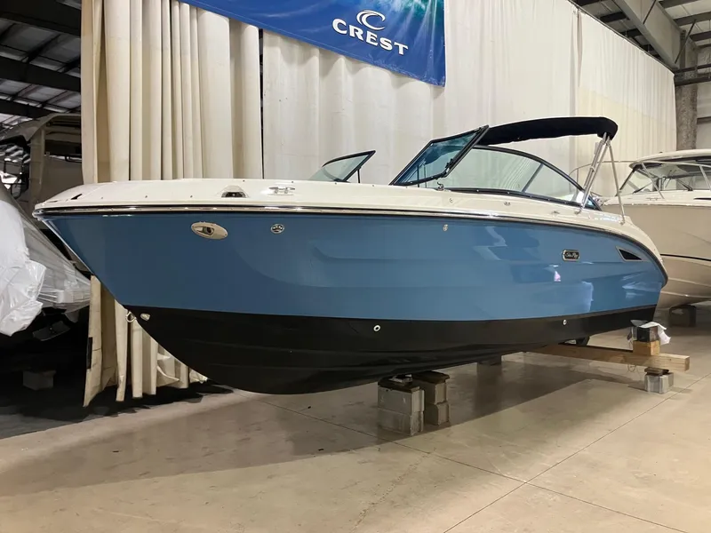 The Image of 2025 Sea Ray SDX 250 boat in showroom, blue hull, black bottom, under Crest banner. - 0