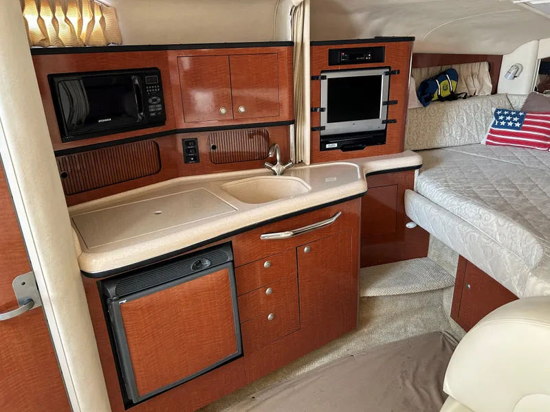 Slide: The Image of Interior of 2005 Sea Ray 300 Sundancer with kitchenette, bed, and American flag pillow. - 14