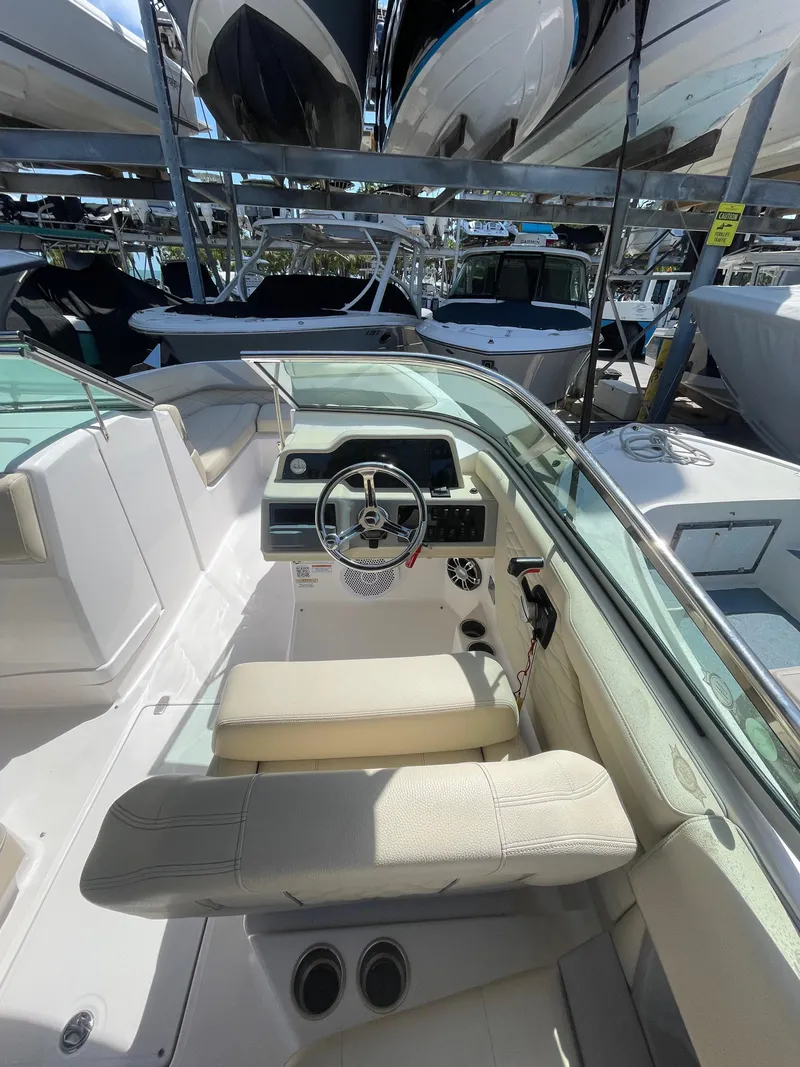 Slide: The Image of 2021 Regal 260BX boat interior with steering wheel and seating, docked among other boats. - 12