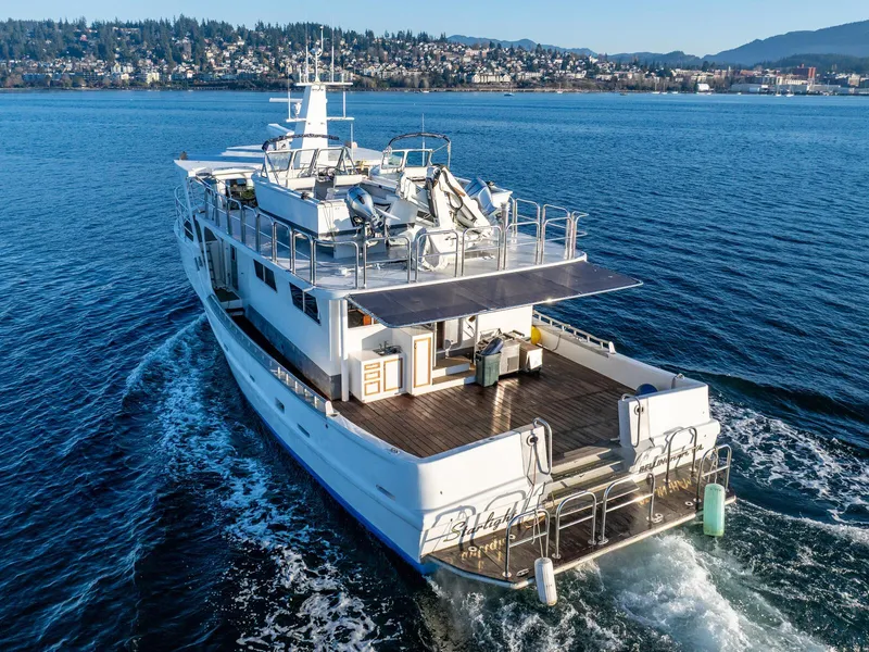 Slide: The Image of Custom Expedition Vessel 58, 1986, cruising on a scenic waterway with cityscape in the background. - 2