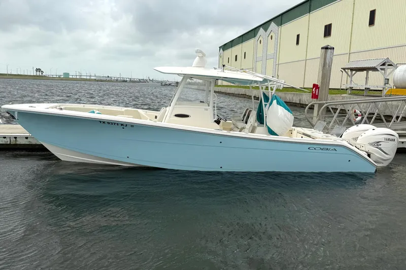 Slide: The Image of 2020 Cobia 320 Center Console boat docked in marina, light blue hull, overcast sky. - 1