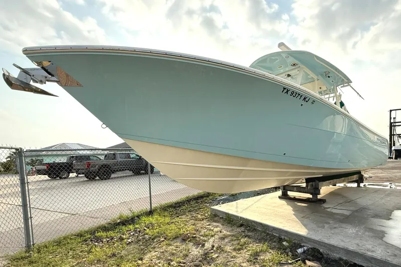 Slide: The Image of 2020 Cobia 320 Center Console boat on display, light blue hull, parked near a fence. - 3