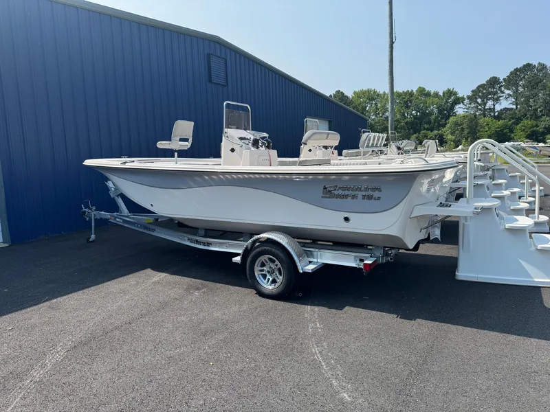 Slide: The Image of 2025 Carolina Skiff 19 LS boat on trailer, parked near blue building. - 2