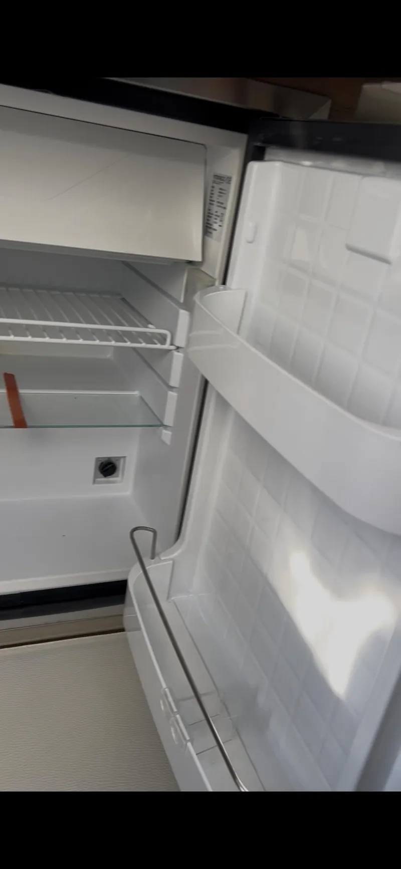 Slide: The Image of Open refrigerator inside a 2020 Cruisers Yachts 338OB, showing shelves and door storage. - 25