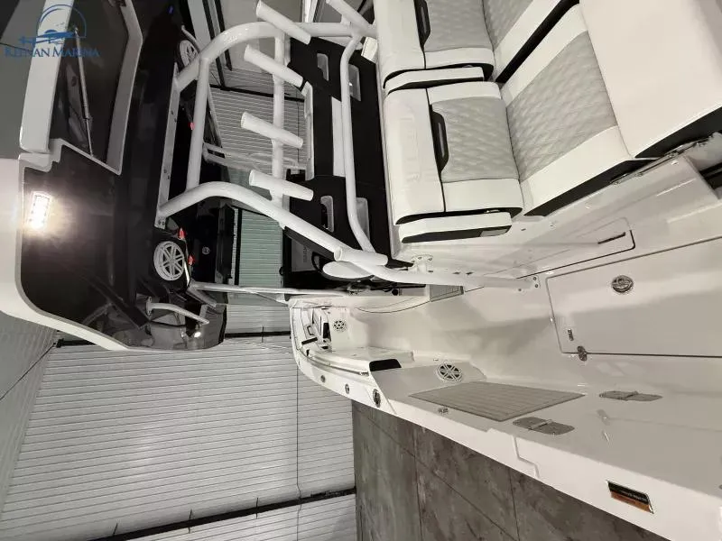 Slide: The Image of 2025 Blackfin 332 CC boat interior with white seating and rod holders in a storage facility. - 7