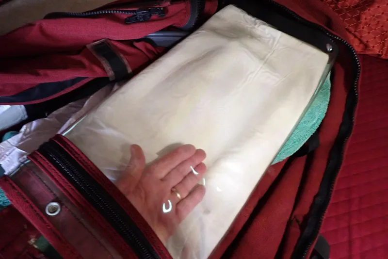 Slide: The Image of A hand packing a red bag with a folded white item inside. - 33