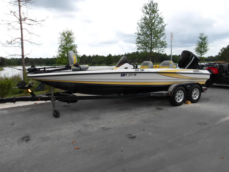 Slide: The Image of 2006 Triton 20X2 boat on trailer, parked near a lake with trees in the background. - 0