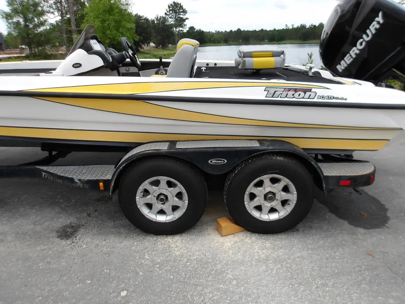 Slide: The Image of 2006 Triton 20X2 boat on trailer with Mercury engine, parked near a lake. - 2