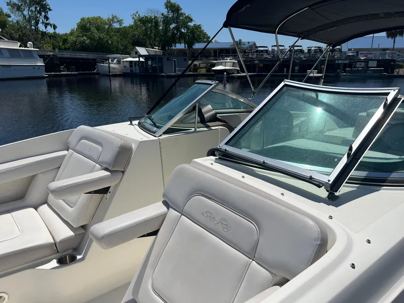 Slide: The Image of 2012 Sea Ray 260 Sundeck boat interior with white seating and windshield, docked by the water. - 17