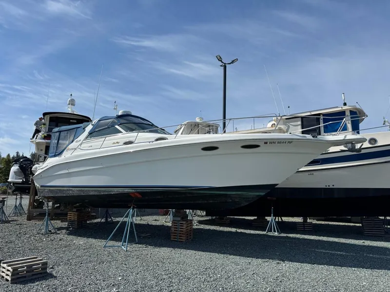 The Image of 1997 Sea Ray 330 Sundancer boat on stands, displayed outdoors under a clear sky. - 0