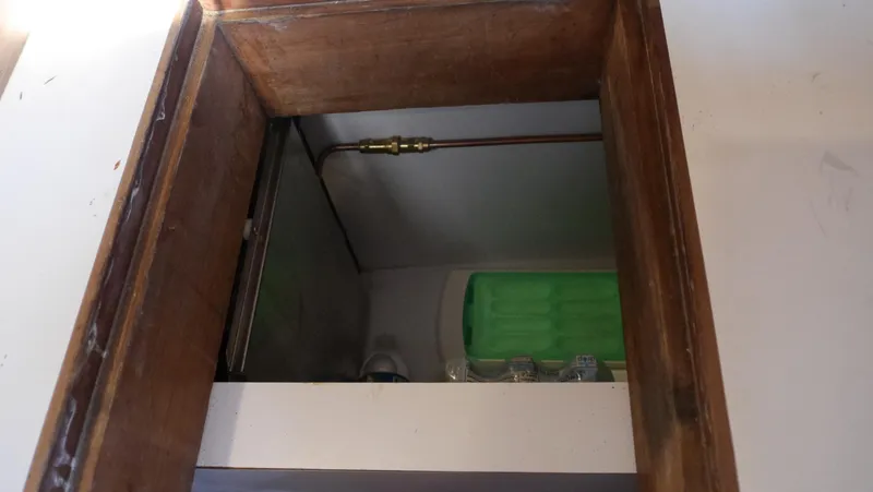Slide: The Image of Wooden hatch with visible plumbing and green storage inside Tayana 37, 1979 model. - 34