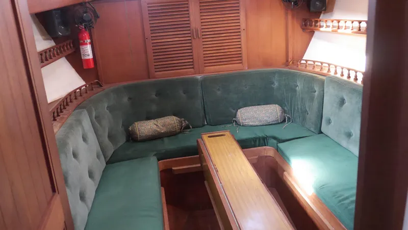 Slide: The Image of 1979 Tayana 37 yacht interior with green cushioned seating and wooden table. - 39