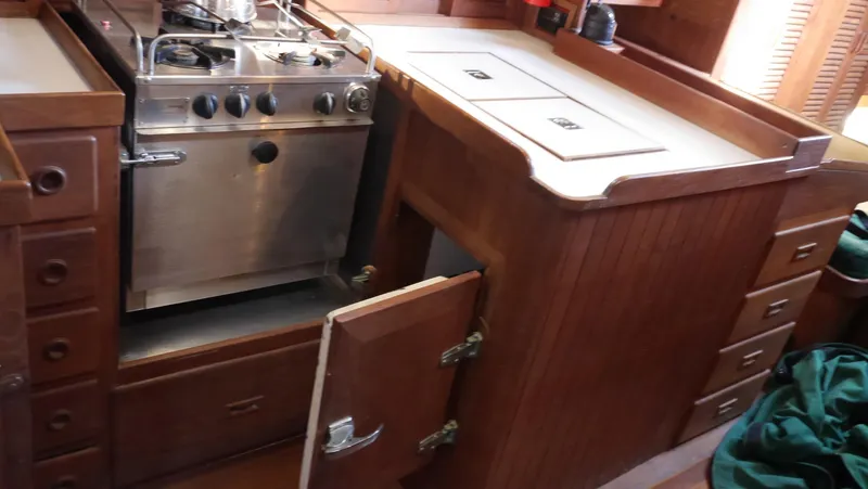 Slide: The Image of 1979 Tayana 37 yacht kitchen with stove, wooden cabinets, and storage compartments. - 37