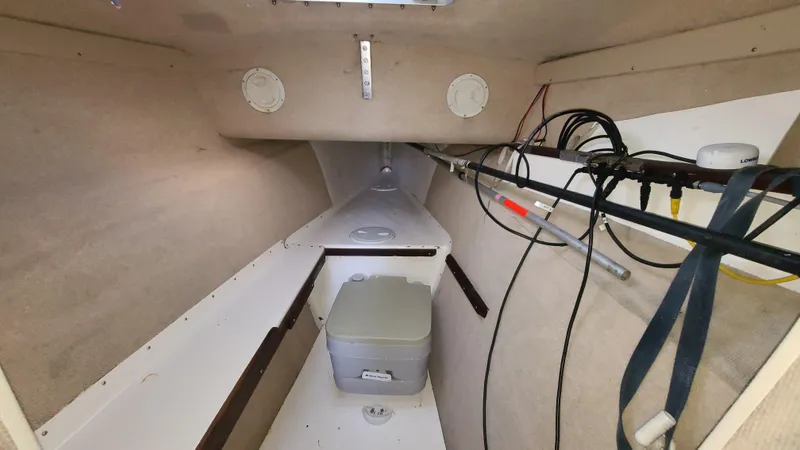 Slide: The Image of Interior of 1987 Corsair F-27 sailboat, featuring compact cabin space with portable toilet. - 12