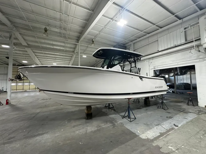 Slide: The Image of 2025 Blackfin 272CC boat in a warehouse, elevated on stands. - 1