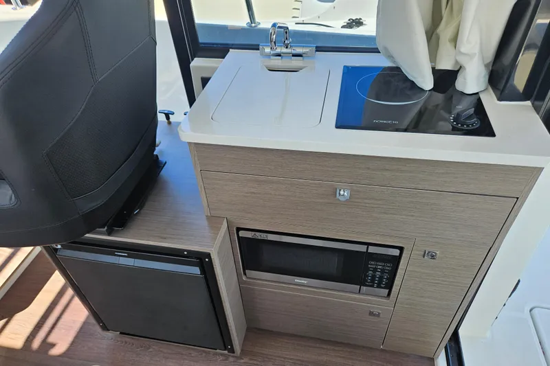 Slide: The Image of Compact kitchen area in 2026 Jeanneau NC 895 Sport Series 2 boat, featuring sink, stove, and microwave. - 13