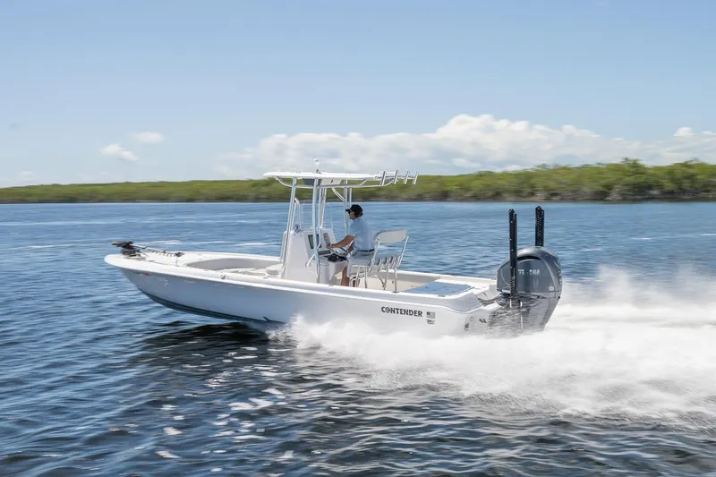 Slide: The Image of 2024 Contender 26 Bay boat speeding on water, clear sky, lush greenery in background. - 2