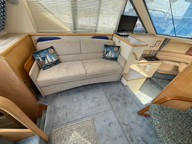 Slide: The Image of 1996 Carver 325 Aft Cabin interior with beige sofa, nautical pillows, and compact entertainment area. - 14
